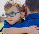 An autistic child wearing glasses being held by his father in a blue pocka-dot shirt.